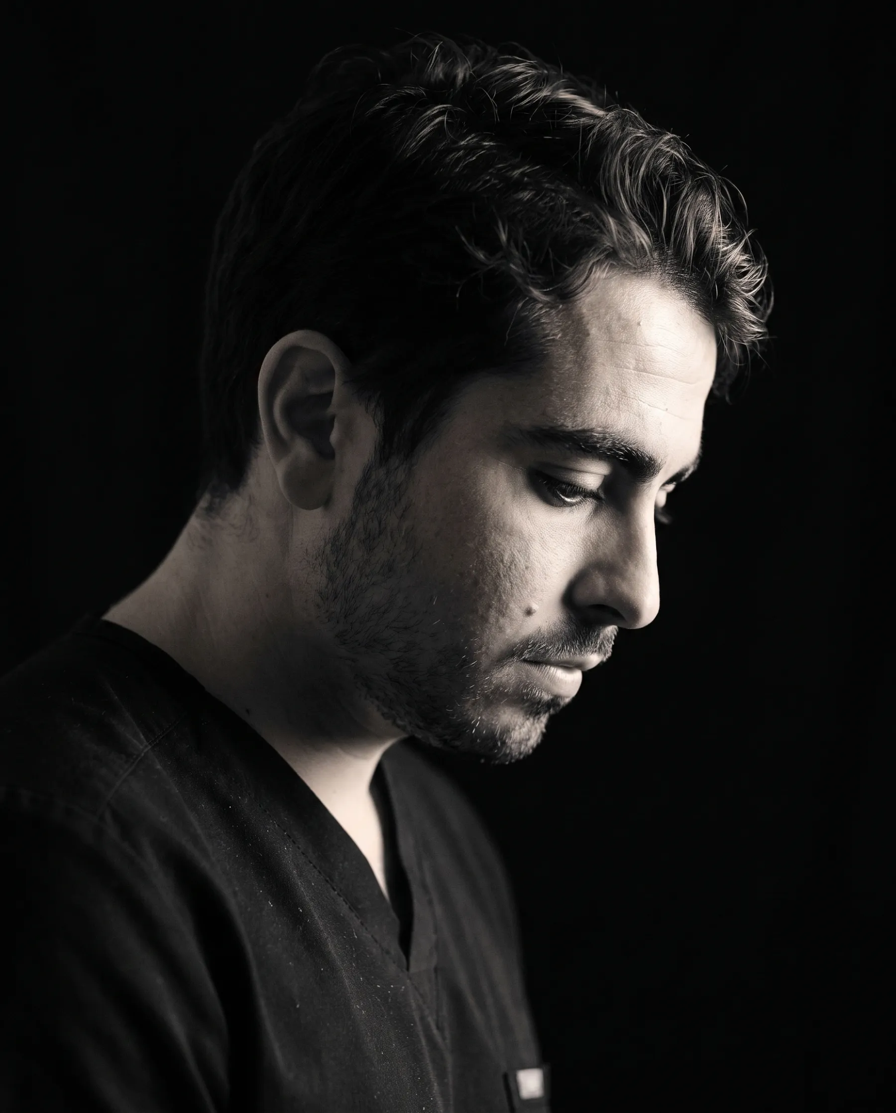 Portrait de profil du Dr Eliav Ayache, regard baissé, sur fond noir